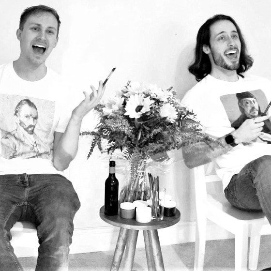 Two men in white t-shirts and blue jeans singing while holding paintbrushes. Between them sits a bunch of sunflowers on a little table.